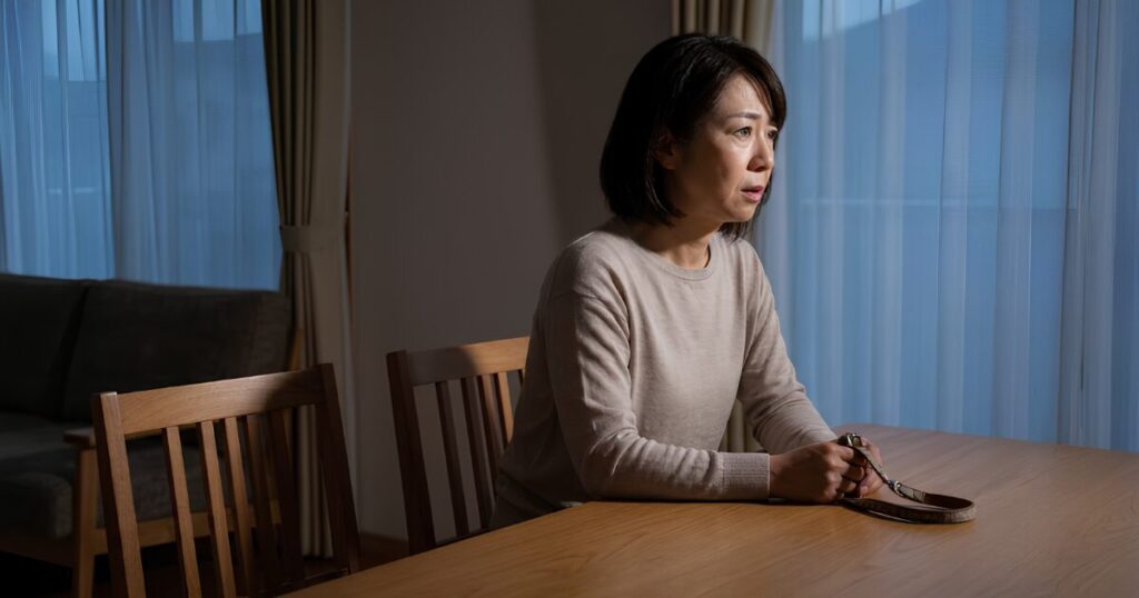 暗い部屋で一人、リードを手に不安な表情を浮かべる日本人の高齢女性。飼い主亡き後のペットの行き場のない不安を表現。