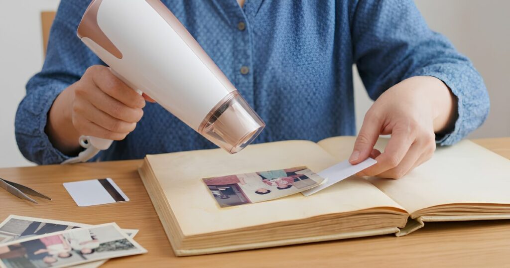 古い粘着式のアルバム台紙から、ドライヤーの温風とプラスチックカードを使い、写真を傷つけずに慎重に剥がす日本人女性の手元
