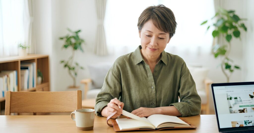 自宅のリビングで穏やかな表情でエンディングノートに書き込みをする、終活を始めた日本人の独身女性。